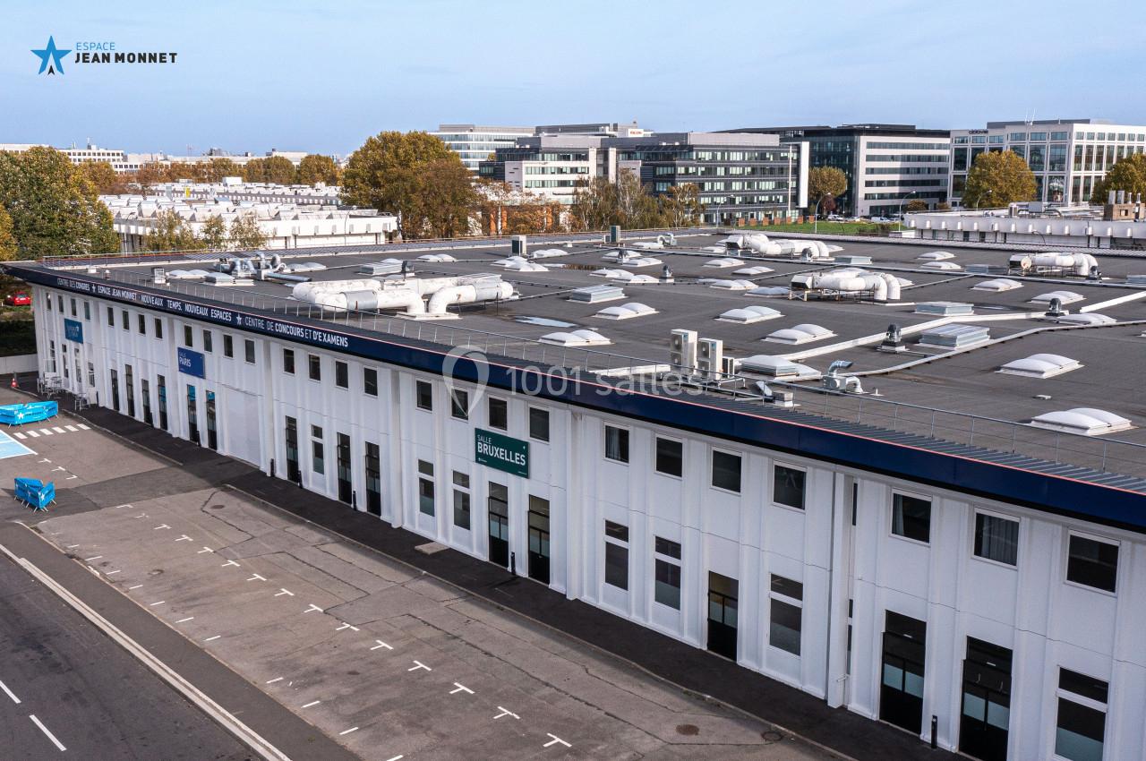 Vue aérienne d'un grand bâtiment blanc avec un toit plat, entouré d'arbres et de structures modernes.