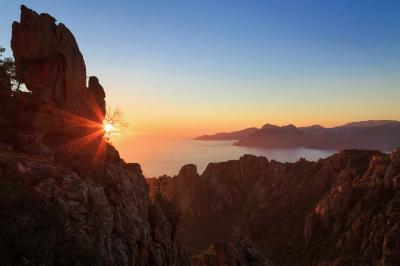 Miniature Corsica Convention Bureau #8 Paysage montagneux au coucher du soleil avec une personne debout sur un promontoire rocheux, entourée de végétation.