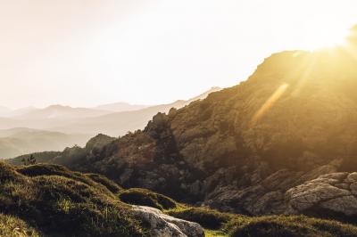 Miniature Corsica Convention Bureau #15 Paysage montagneux au coucher du soleil avec une personne debout sur un promontoire rocheux, entourée de végétation.