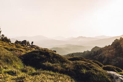 Miniature Corsica Convention Bureau #16 Paysage montagneux au coucher du soleil avec une personne debout sur un promontoire rocheux, entourée de végétation.