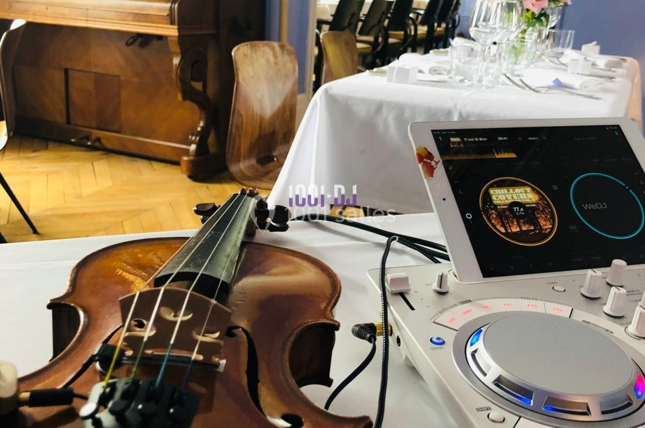 Un violon posé sur une table près d'une console DJ et d'une tablette dans une salle de réception.
