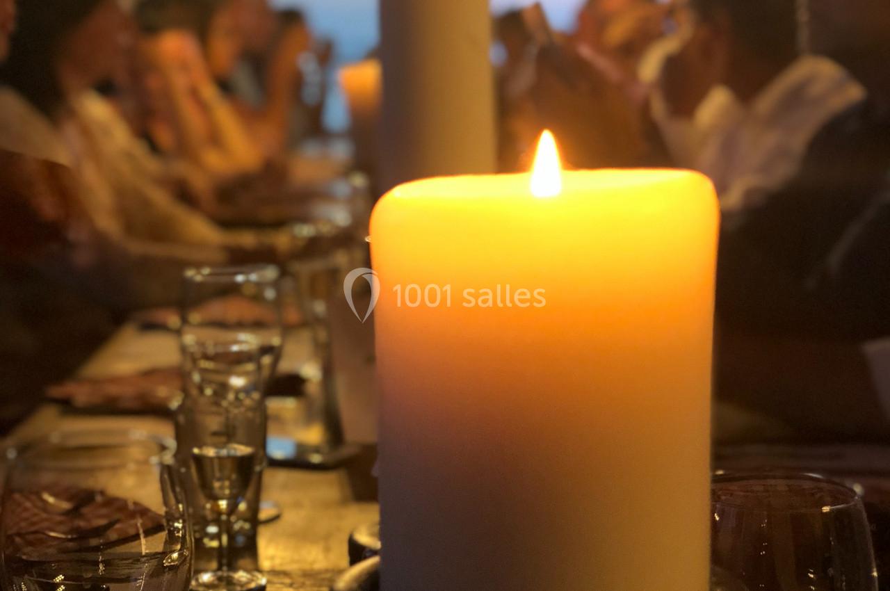 Bougie allumée au centre d'une table entourée de convives flous dans une ambiance chaleureuse et tamisée.