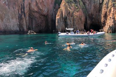 Un bateau pneumatique noir et jaune navigue sur une mer calme, avec une ville et des collines en arrière-plan.