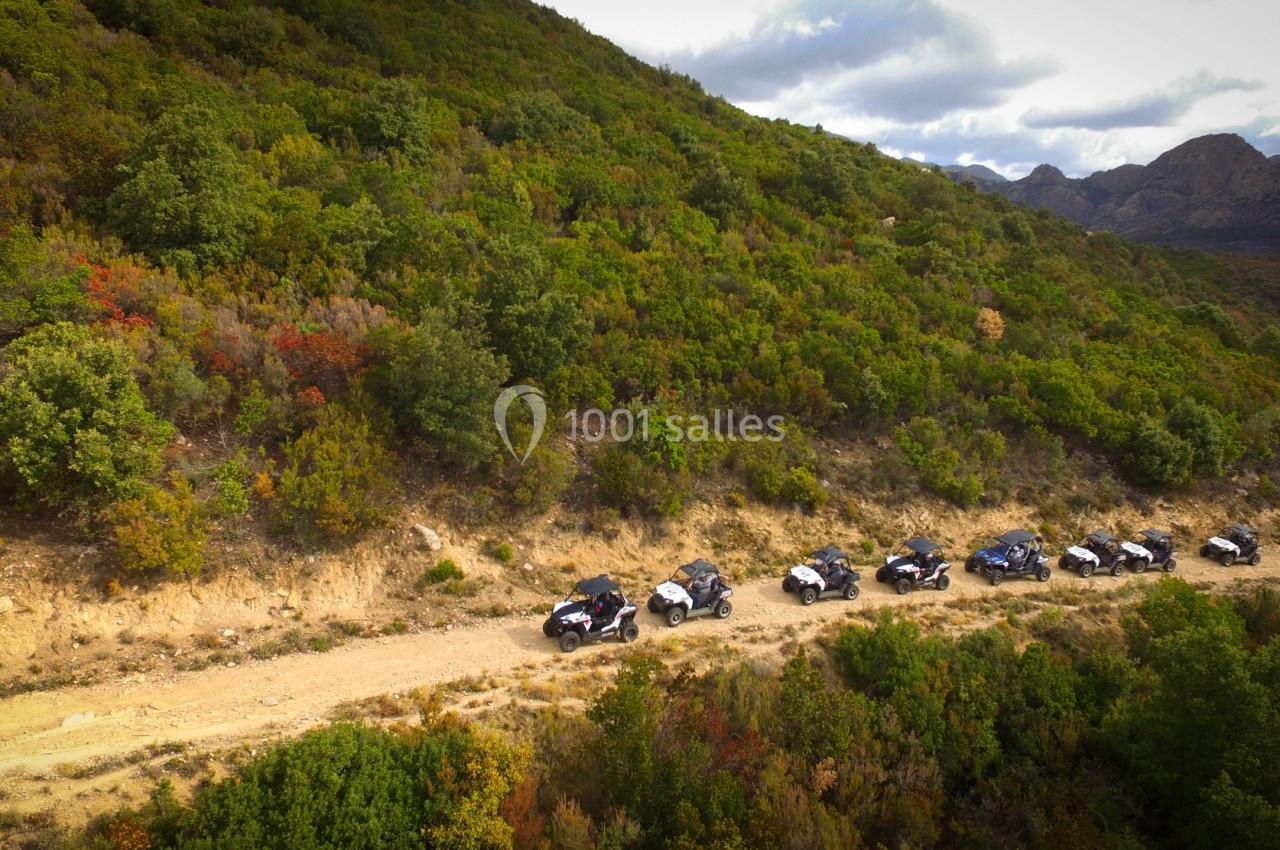 Vue aérienne d'un groupe de véhicules tout-terrain roulant sur un chemin de terre entouré de collines boisées.