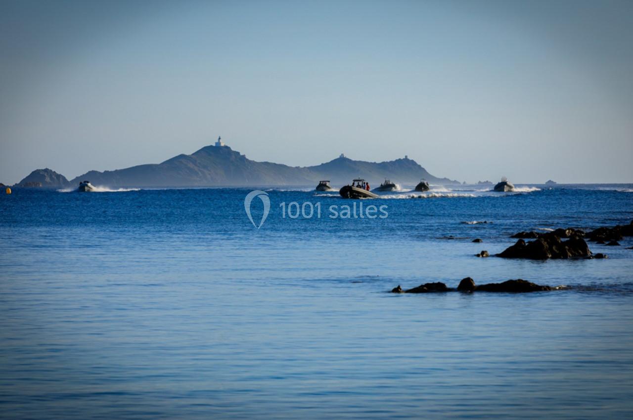 Vue sur une mer calme avec plusieurs bateaux rapides naviguant près d'une île rocheuse à l'horizon.