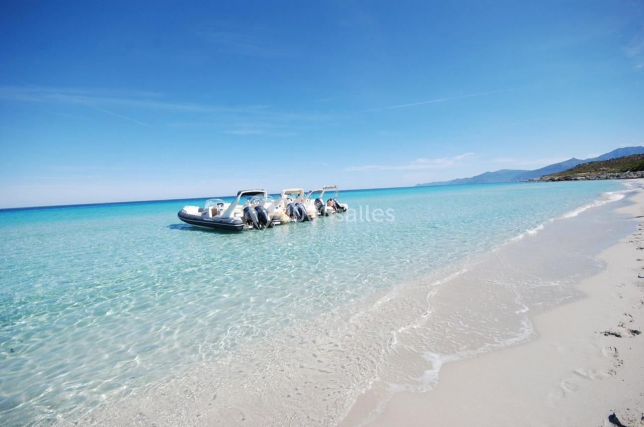 Quatre bateaux pneumatiques amarrés sur une plage de sable blanc, dans une eau turquoise sous un ciel dégagé.