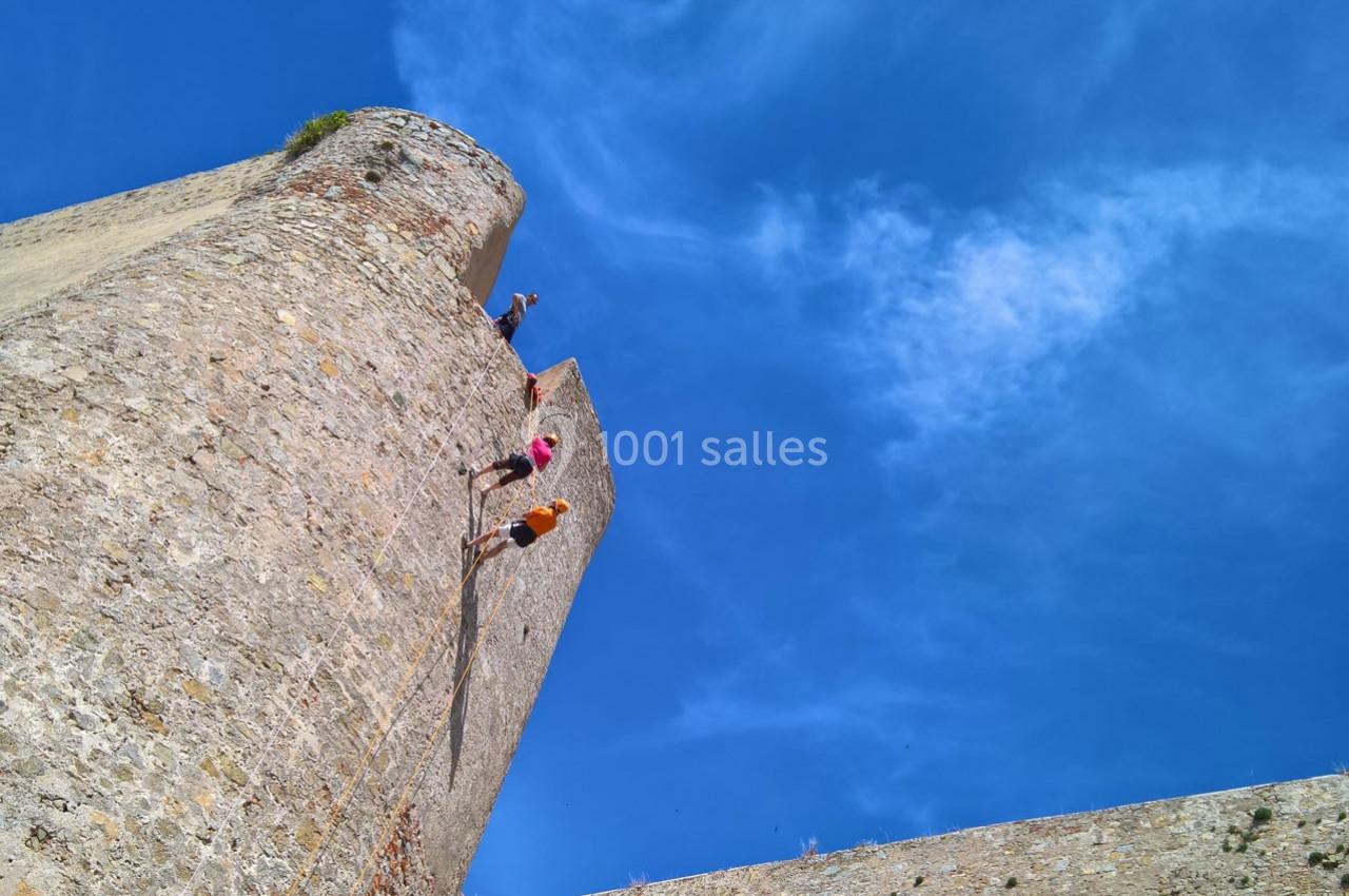 Des personnes escaladent une haute paroi en pierre sous un ciel bleu dégagé.