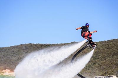 Un homme équipé d'un flyboard s'élève au-dessus de l'eau avec un paysage de collines en arrière-plan.