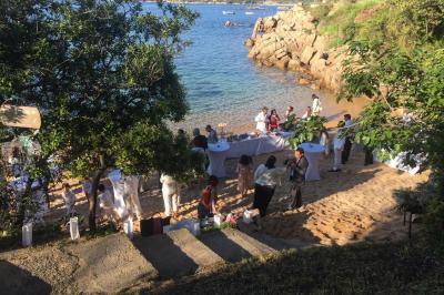 Tente transparente installée sur une plage, aménagée avec des chaises blanches et des plantes décoratives.