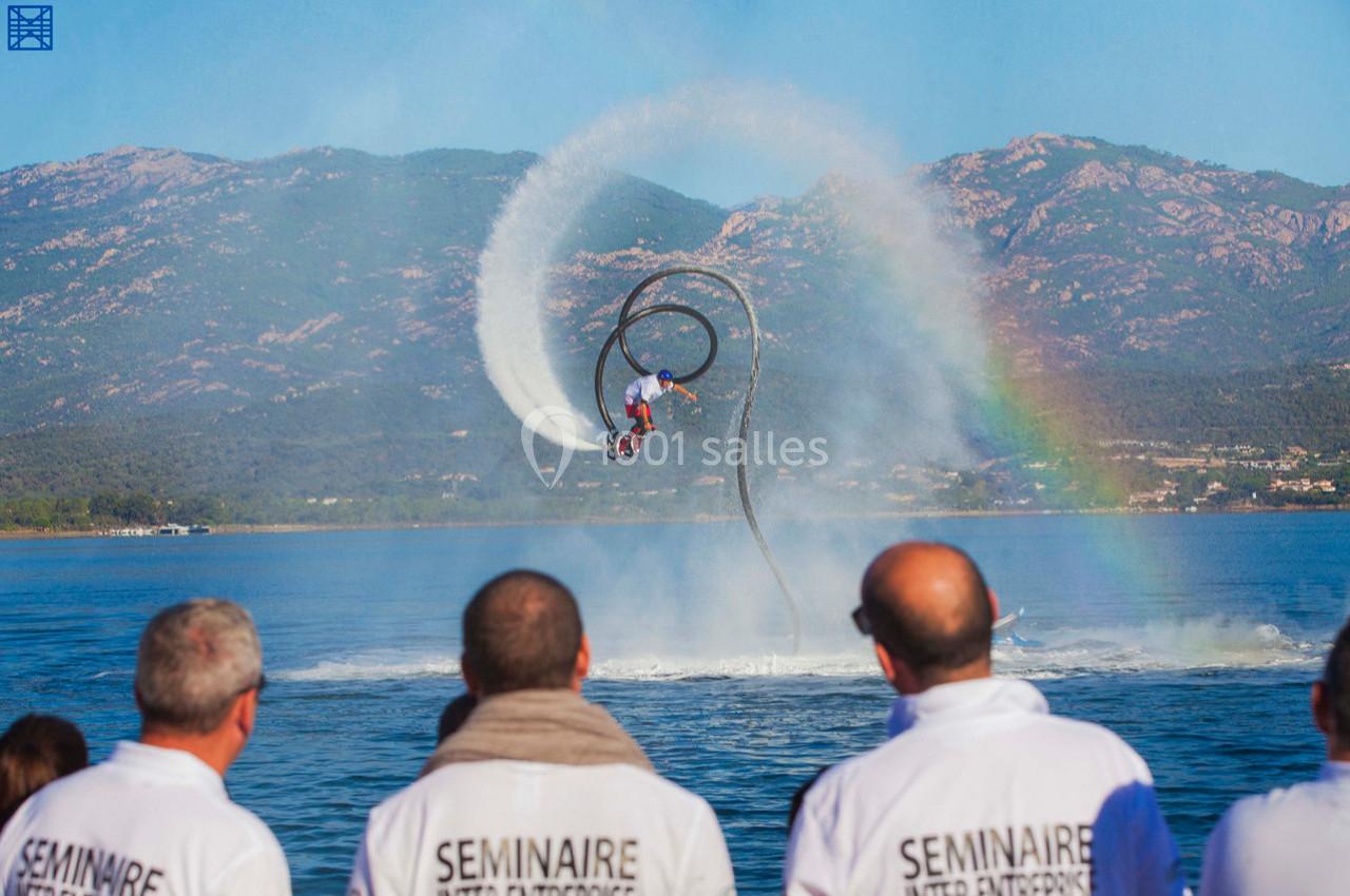 Un homme effectue une figure en flyboard au-dessus de l'eau, sous le regard de spectateurs en chemises blanches.