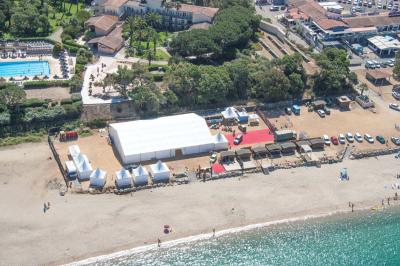 Tente transparente installée sur une plage, aménagée avec des chaises blanches et des plantes décoratives.