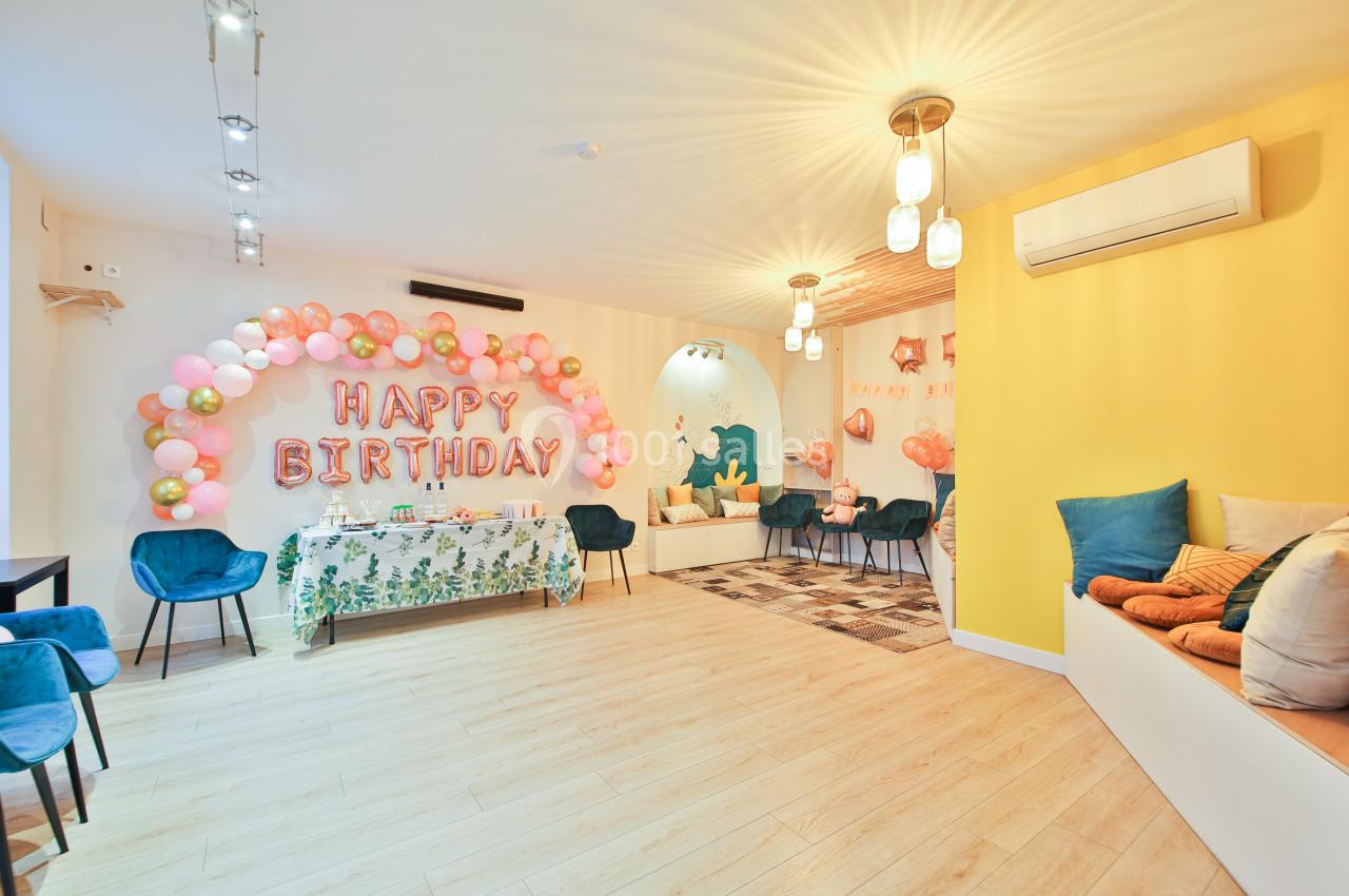 Salle décorée pour un anniversaire avec ballons colorés, guirlandes lumineuses et table ornée de nappes fleuries.