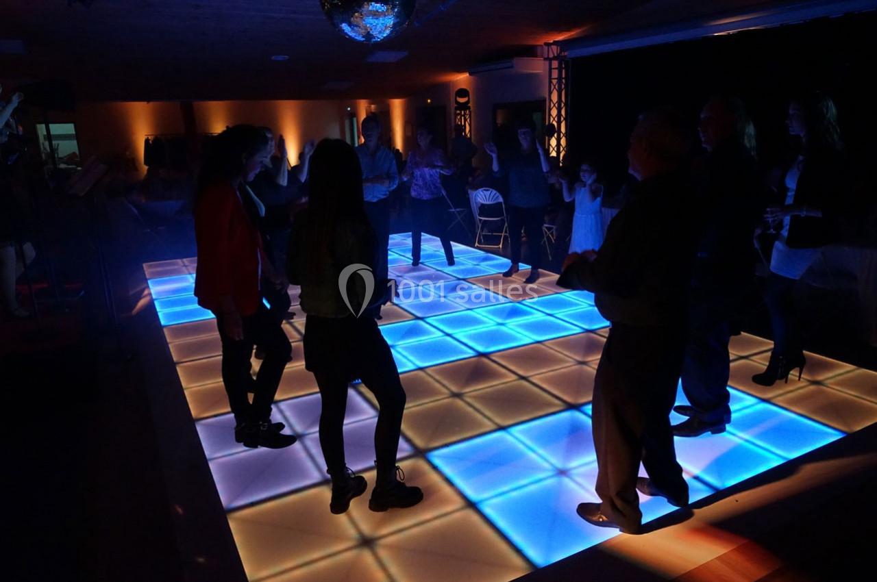 Personnes dansant sur une piste lumineuse à carreaux bleus dans une salle faiblement éclairée.