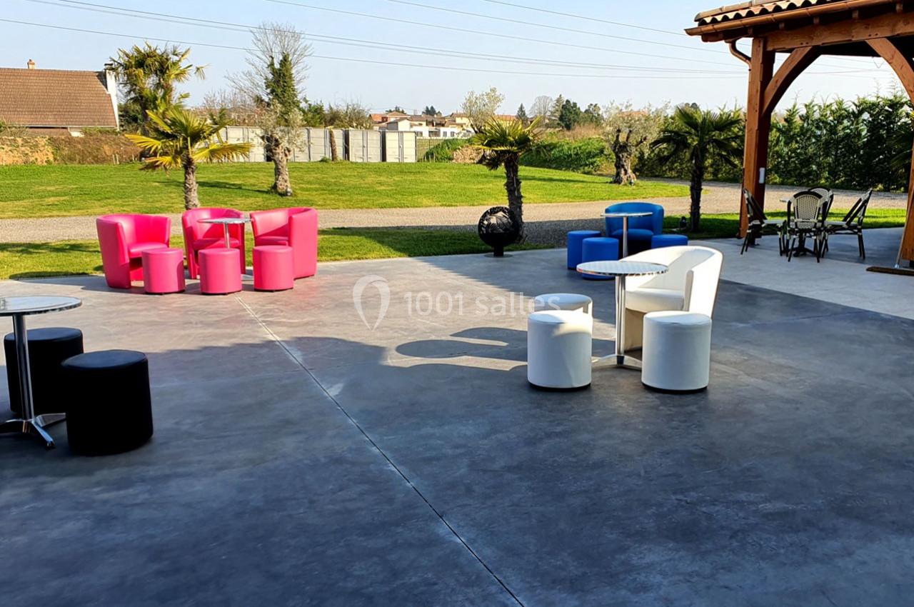 Mobilier coloré disposé sur une terrasse en béton, avec des palmiers et un espace vert en arrière-plan.