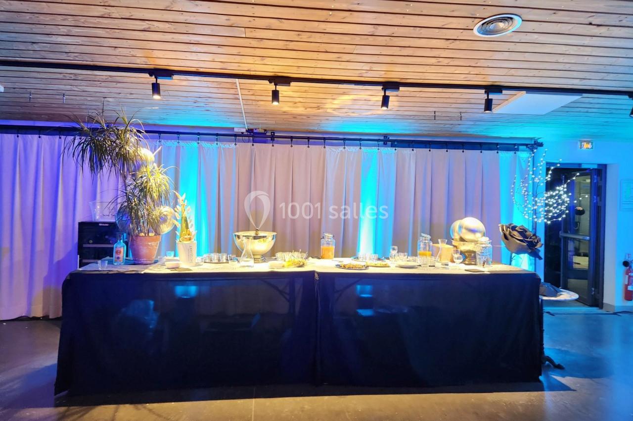 Table de buffet décorée avec des plantes, des lumières et des plats, dans une salle éclairée par des lumières bleues.