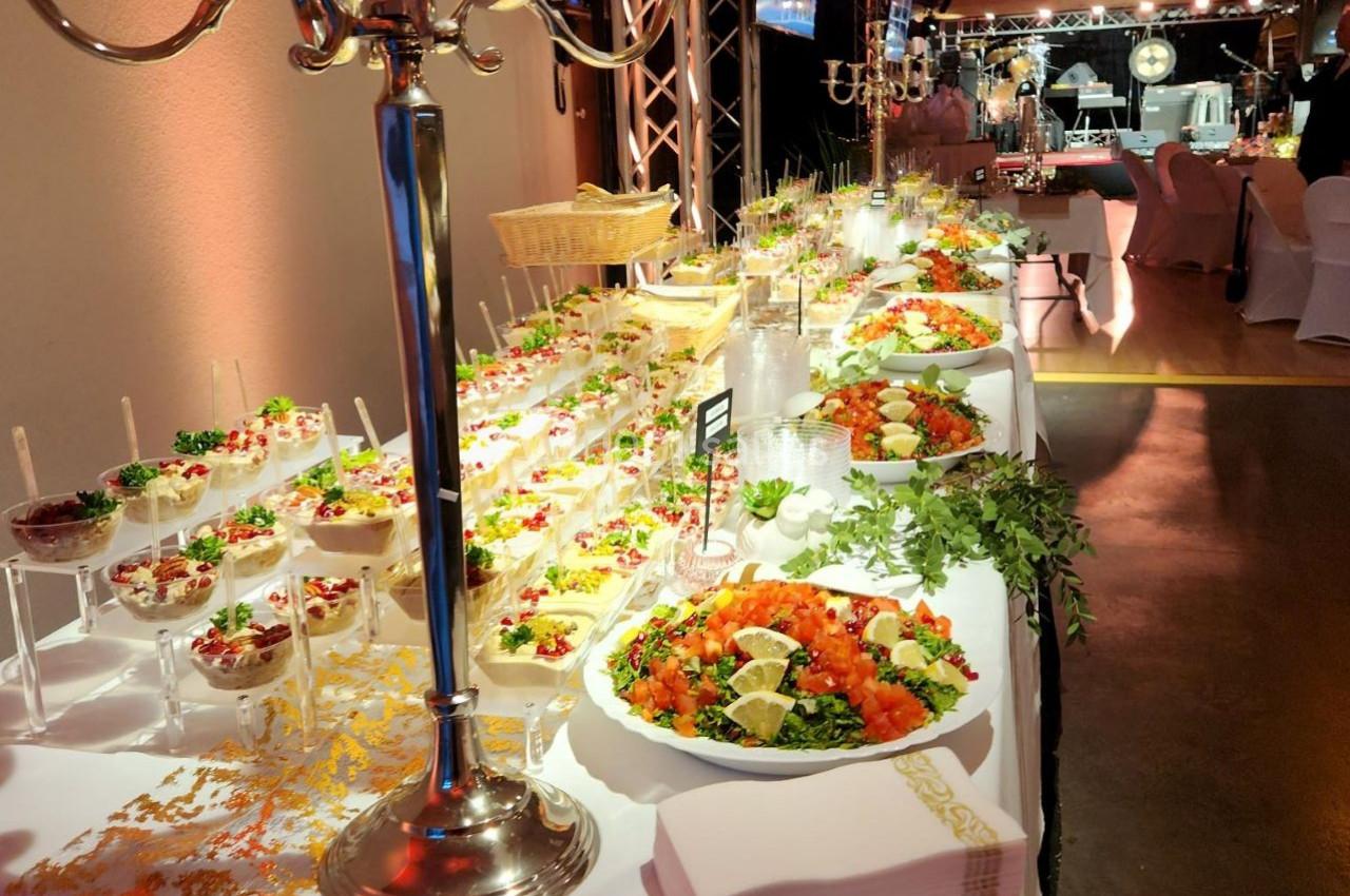 Buffet élégant avec plats variés, salades, verrines et décorations raffinées sous un éclairage chaleureux.