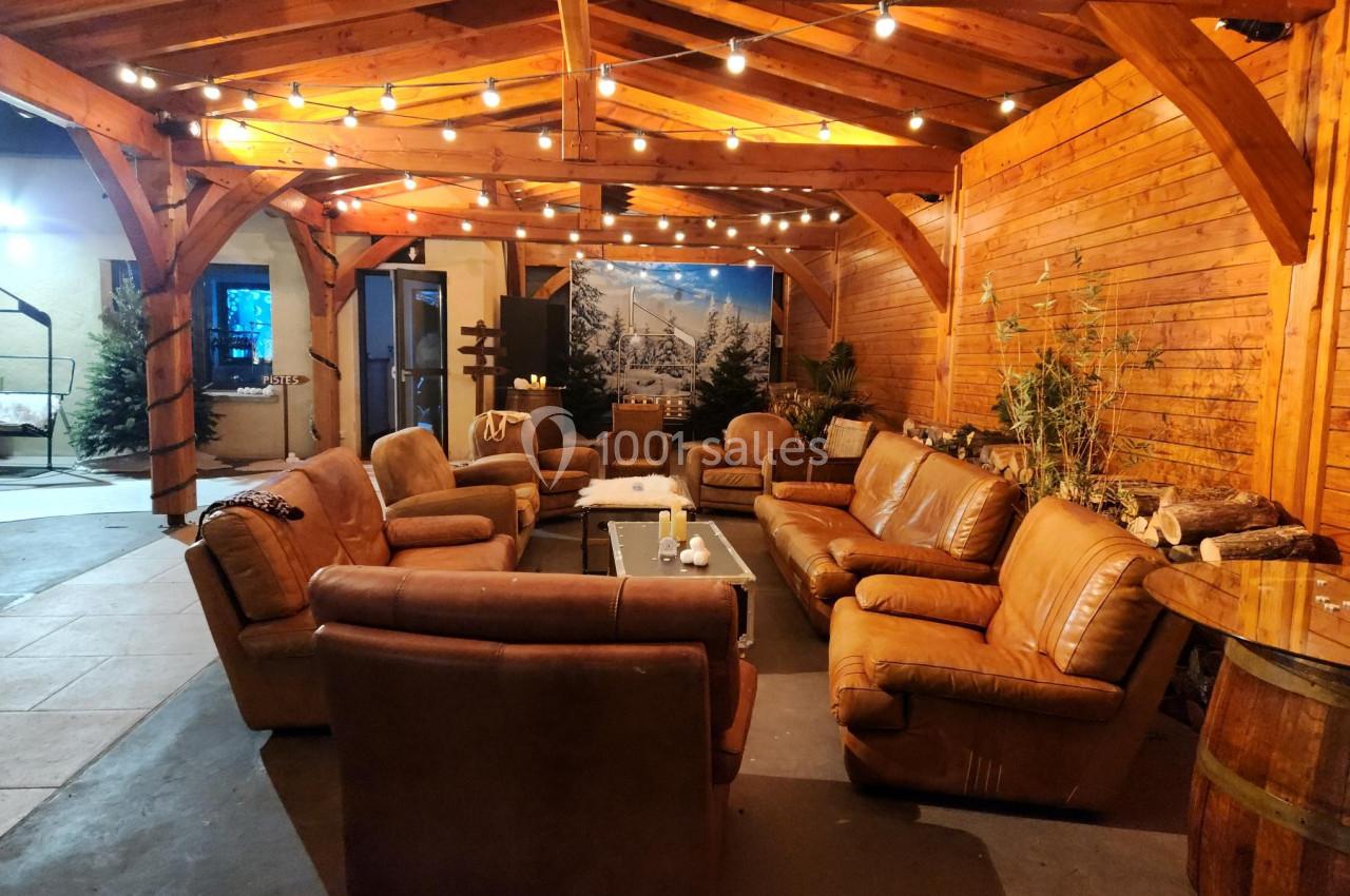 Salon chaleureux sous une pergola en bois, avec canapés en cuir, guirlandes lumineuses et décor montagnard.