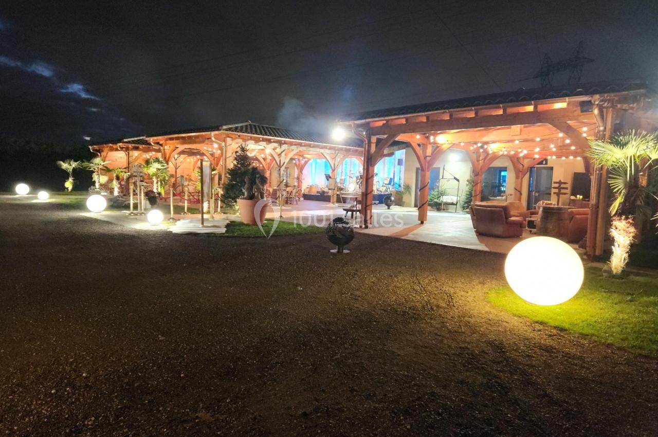 Terrasse éclairée d'un bâtiment en bois avec des lumières décoratives et des sphères lumineuses dans un cadre nocturne.