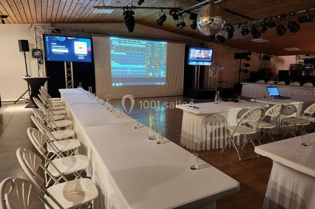 Salle de conférence équipée de tables, chaises, écrans de projection et matériel audiovisuel, prête pour un événement.