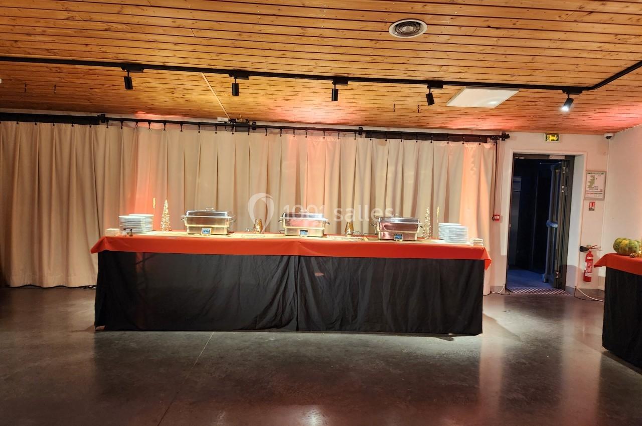 Buffet avec plats chauds sous cloches en métal, assiettes empilées et nappe rouge dans une salle au plafond en bois.
