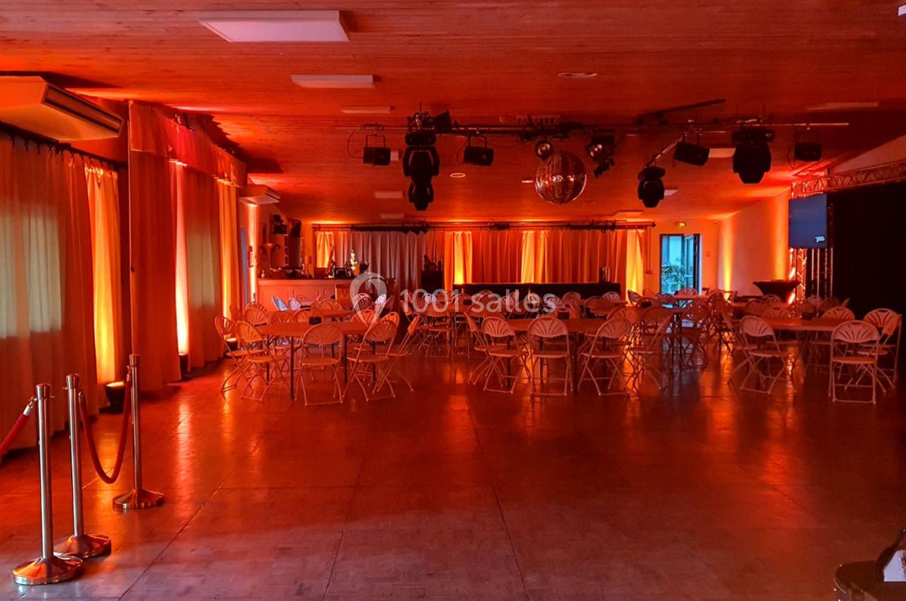 Salle de réception avec tables et chaises disposées, éclairage tamisé orange et boule disco suspendue.