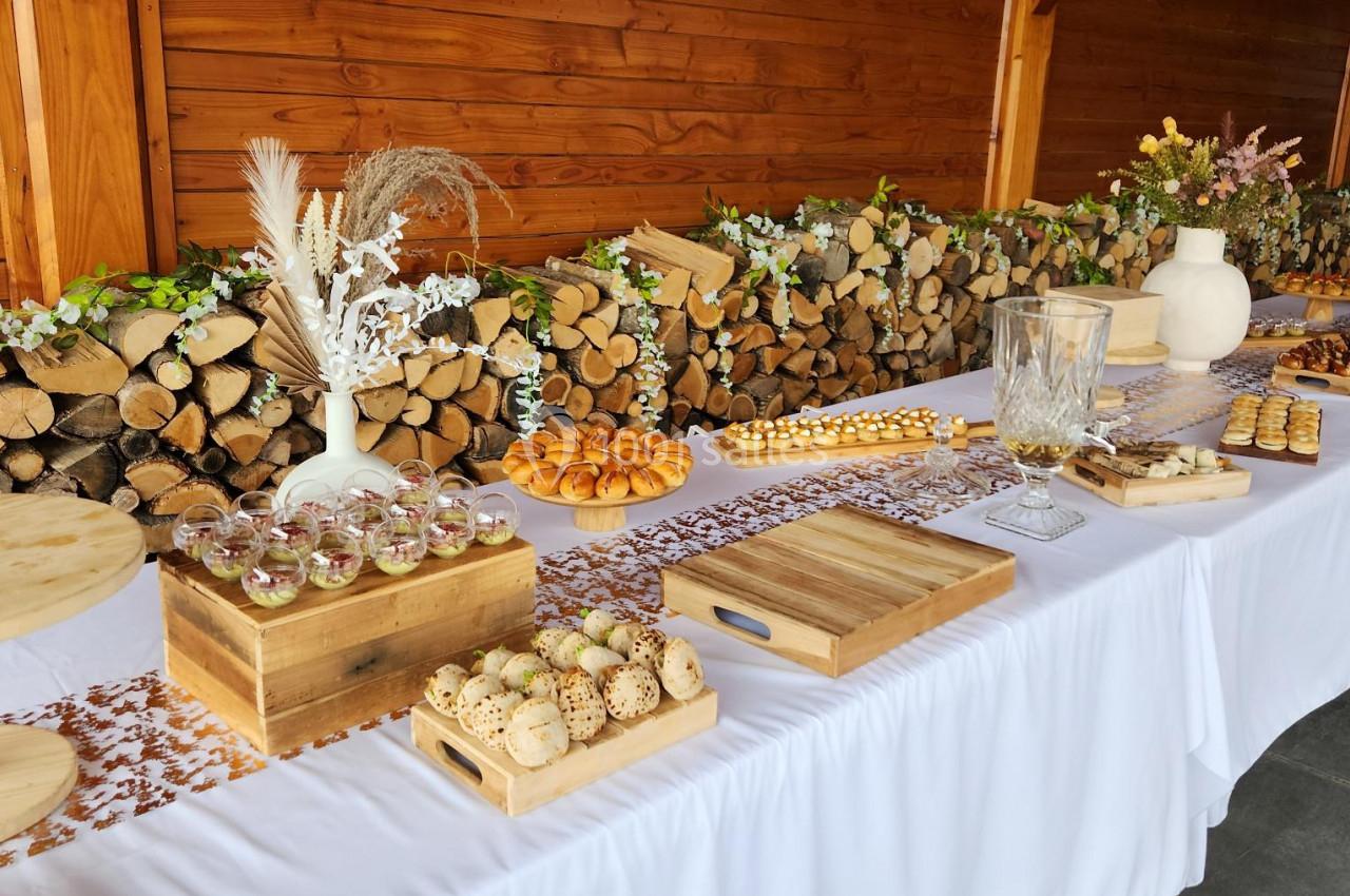 Table de buffet décorée avec des desserts variés, sur fond de mur en bois et de bûches empilées.