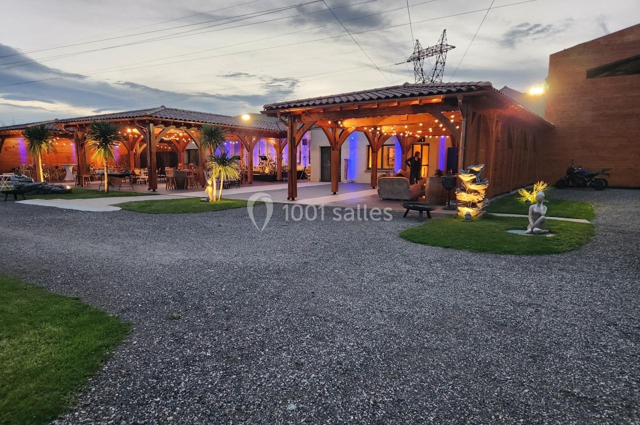 Terrasse éclairée en soirée avec des structures en bois, des plantes décoratives et un ciel partiellement nuageux.