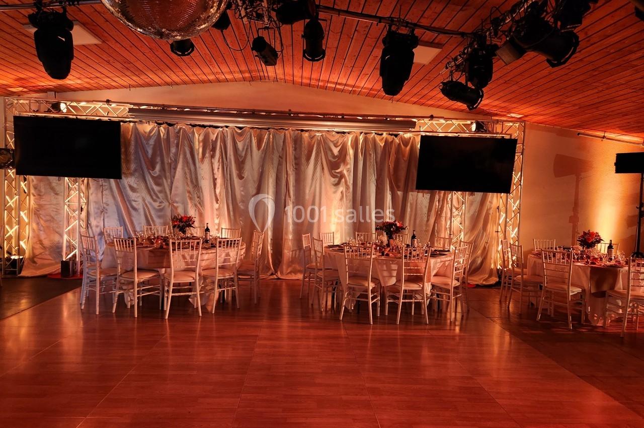 Salle de réception décorée avec des tables dressées, des chaises blanches et un éclairage chaleureux.
