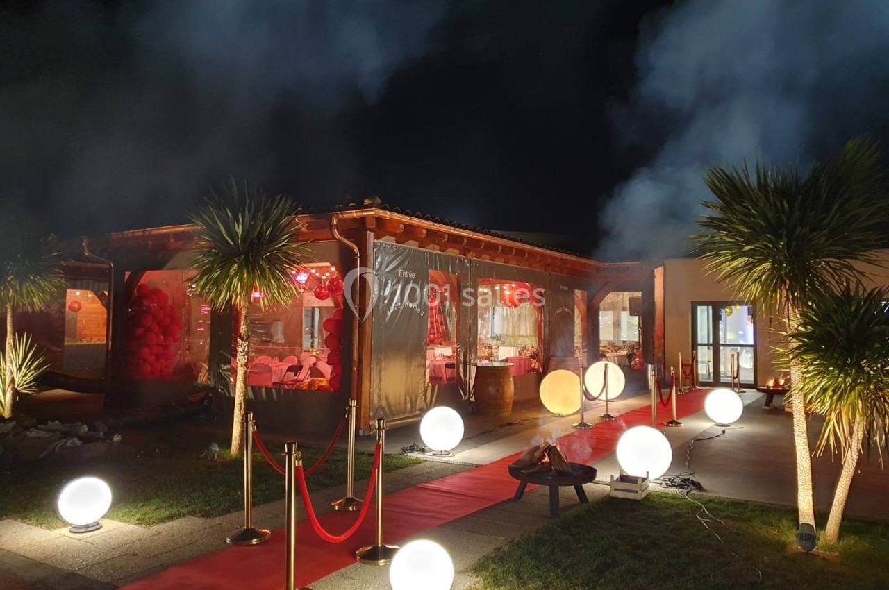 Extérieur d'un bâtiment éclairé la nuit, décoré de lanternes rouges, tapis rouge et lumières sphériques au sol.