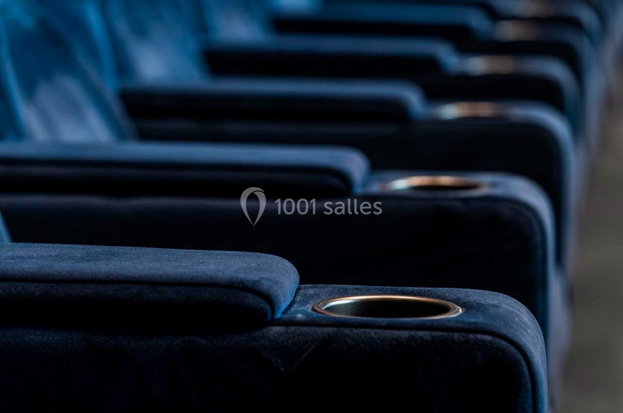 Rangée de sièges de cinéma en velours bleu avec accoudoirs et porte-gobelets intégrés.