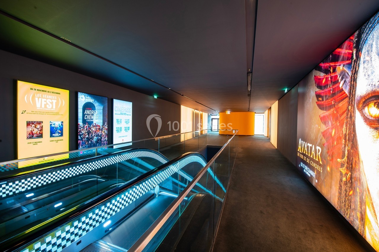 Couloir moderne avec escalators, affiches de films lumineuses sur les murs et éclairage tamisé.