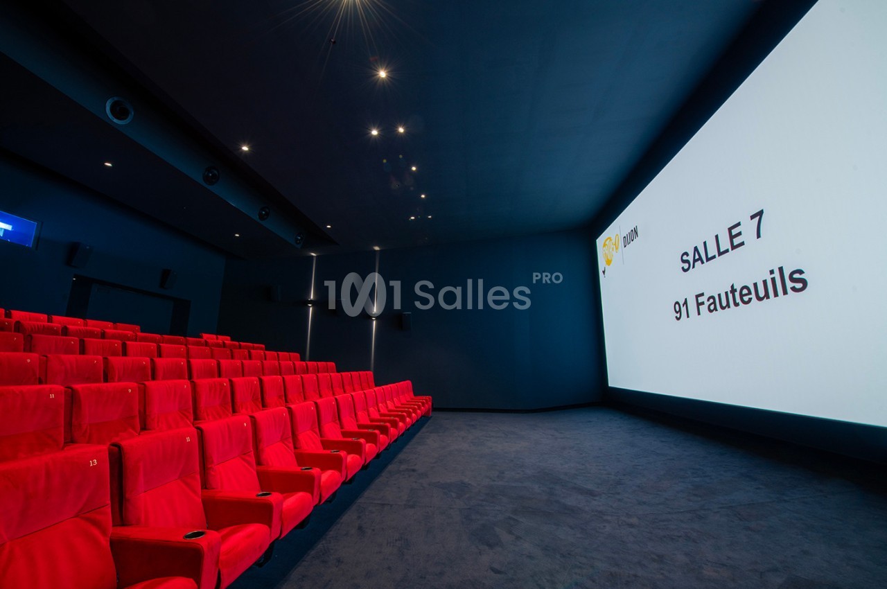 Salle de cinéma vide avec des fauteuils rouges, un écran affichant ’Salle 7, 91 fauteuils’ et un éclairage tamisé.