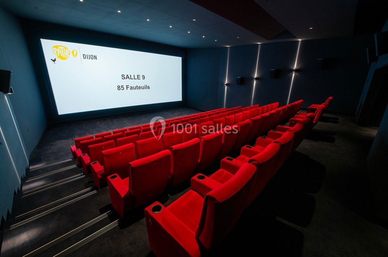 Salle de cinéma vide avec des rangées de fauteuils rouges et un écran affichant ’Salle 9, 85 fauteuils’.