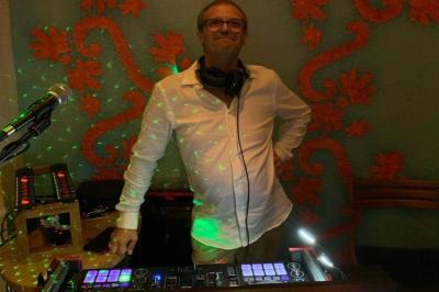 Un DJ mixe derrière une table éclairée par des lumières colorées dans une ambiance de soirée festive.