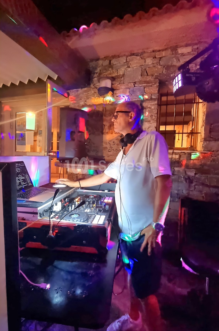 Un DJ mixe de la musique sur une console dans un espace extérieur éclairé par des lumières colorées.