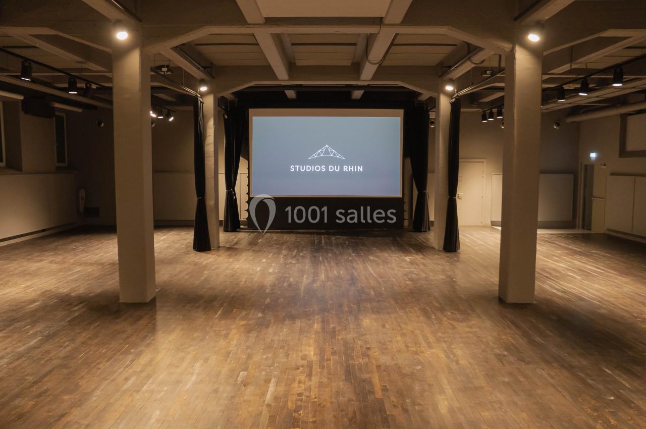 Salle spacieuse avec parquet en bois, écran de projection allumé et éclairage tamisé.