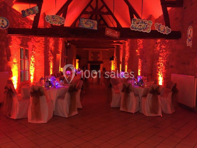 Salle de réception décorée avec des tables dressées, éclairage rouge et guirlandes suspendues au plafond.