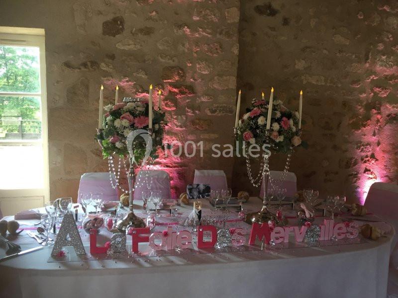 Table de mariage décorée avec des fleurs roses et blanches, bougies allumées et lettres formant ’Au Faire Des Merveilles’.