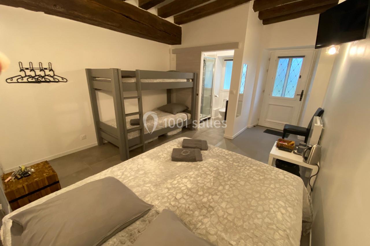 Chambre avec lit double, lits superposés, poutres apparentes, salle de bain attenante et porte-fenêtre.