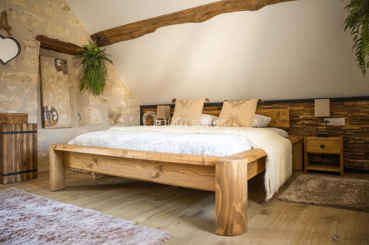 Chambre lumineuse avec lit en bois massif, murs en pierre, poutres apparentes et décorations naturelles.