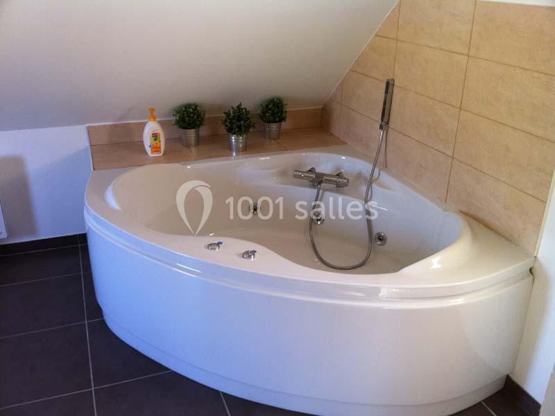 Baignoire d'angle blanche avec robinetterie moderne, entourée de carrelage beige et décorée de plantes vertes.