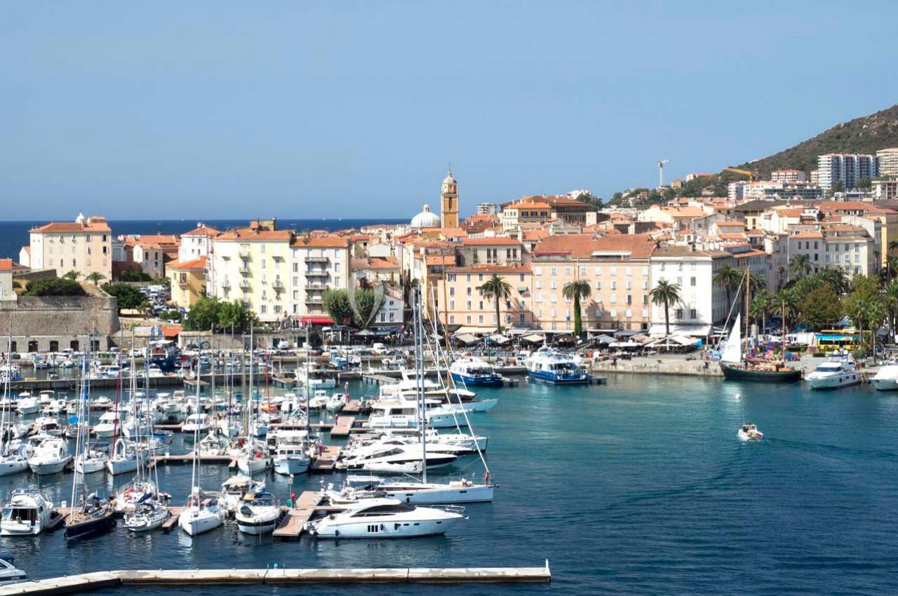 Port avec des voiliers et yachts, bordé par une ville côtière aux bâtiments clairs et collines en arrière-plan.