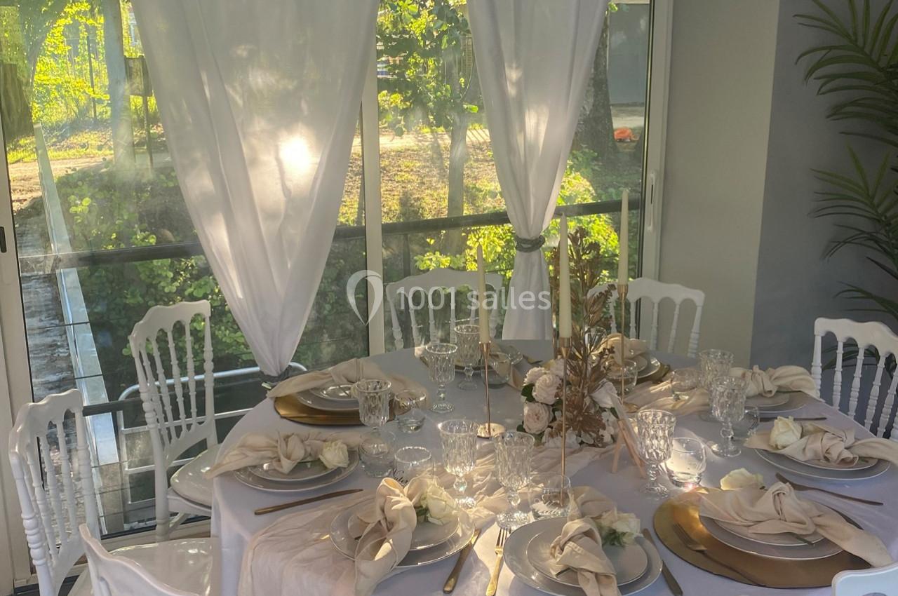 Table élégamment dressée avec nappes blanches, vaisselle raffinée, décor floral et vue sur un jardin ensoleillé.