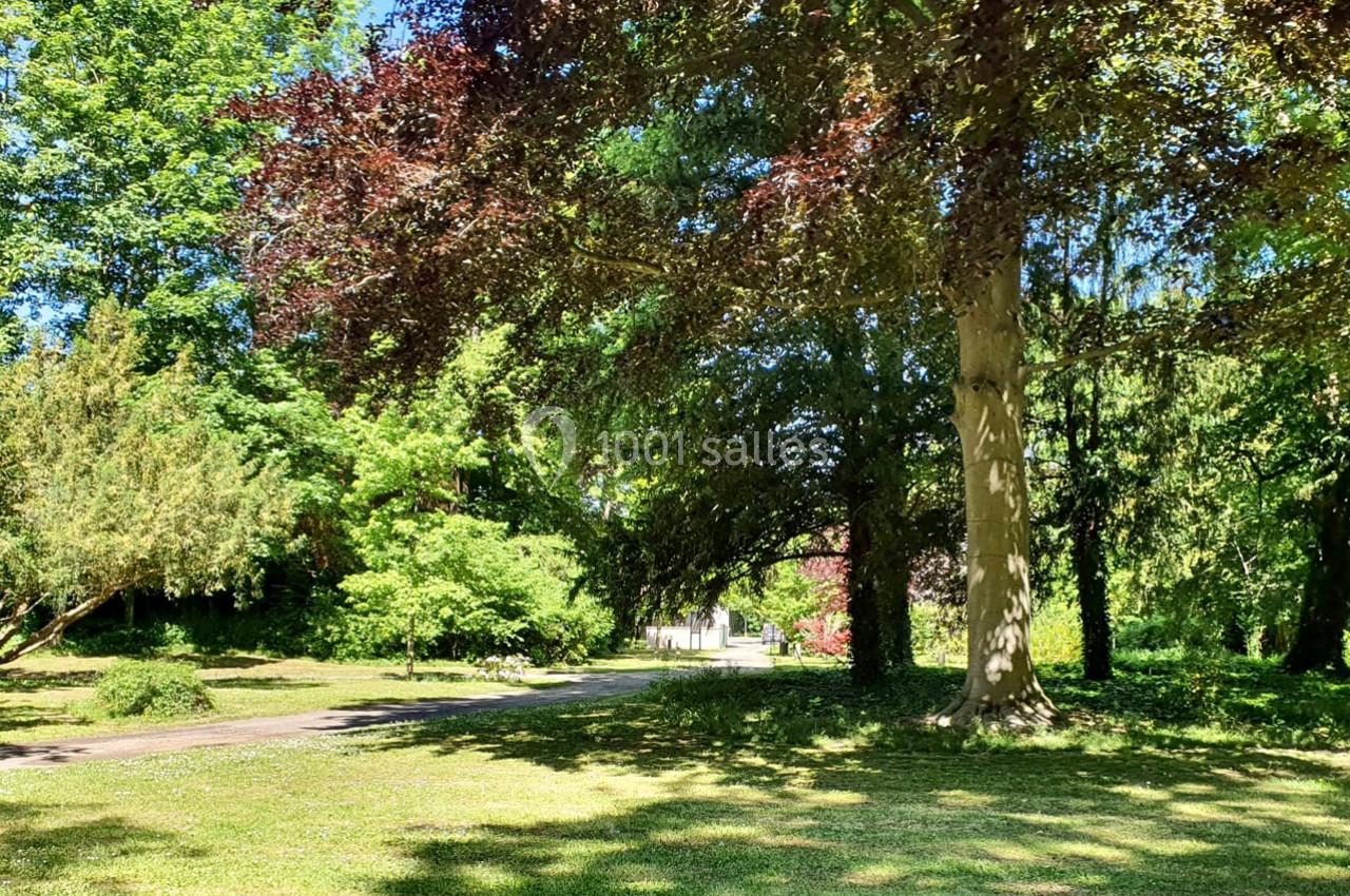 Un parc verdoyant avec des arbres feuillus et une allée ensoleillée menant à un bâtiment blanc au loin.
