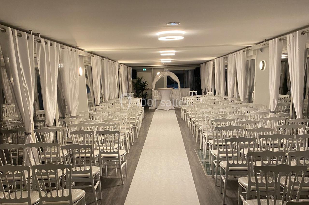 Salle de cérémonie décorée avec des chaises blanches alignées de part et d'autre d'une allée centrale recouverte d'un tapis…