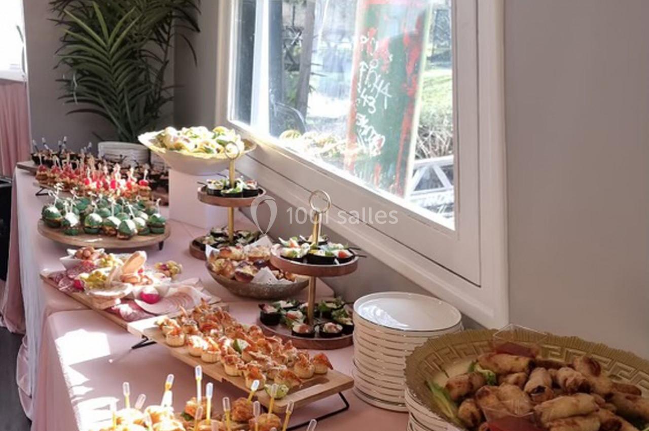 Buffet varié avec des amuse-bouches et plats disposés sur une table près d'une fenêtre lumineuse.