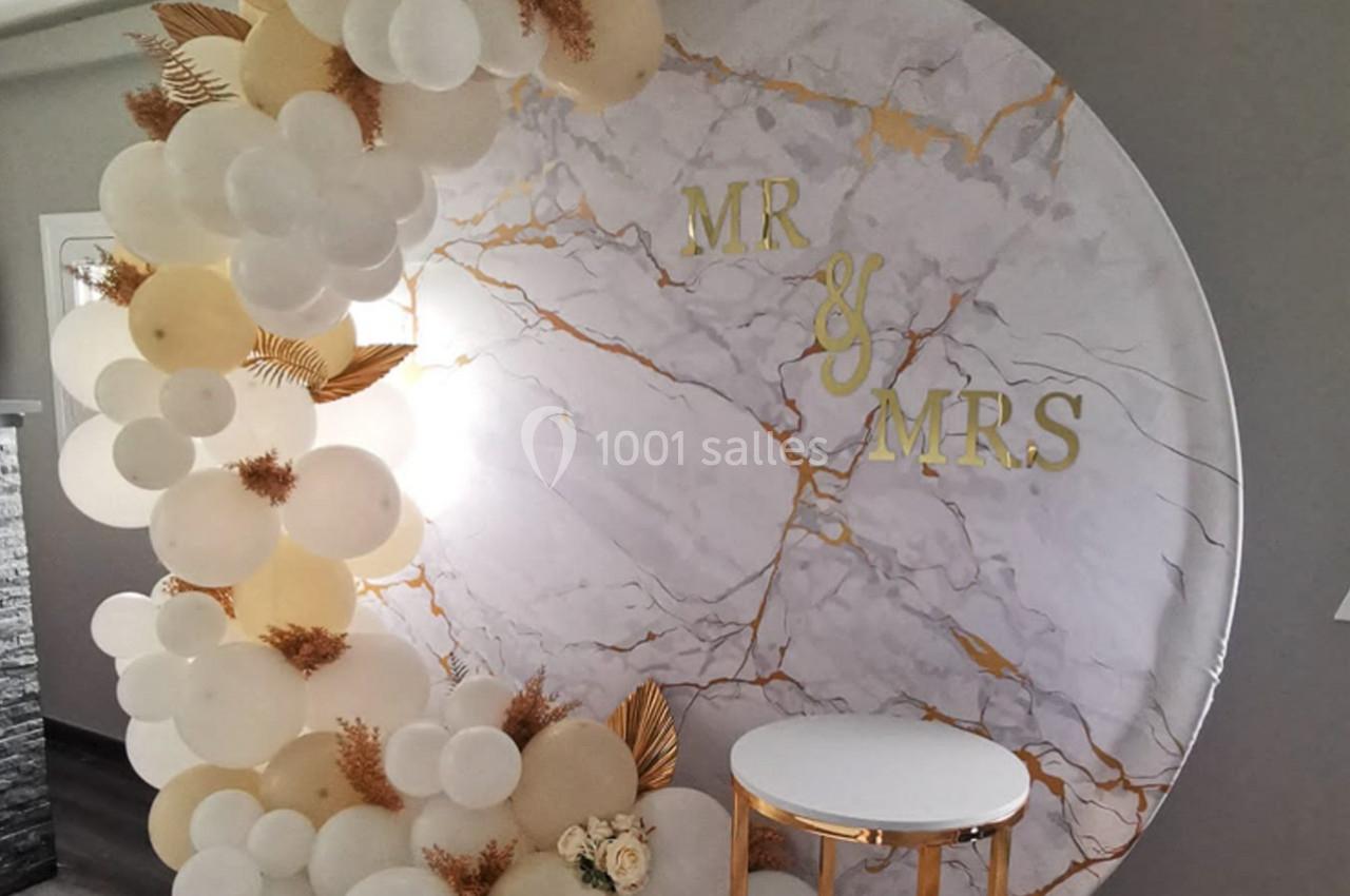 Décor de mariage avec arche de ballons blancs et beiges, fond circulaire marbré et inscription ’Mr & Mrs’.