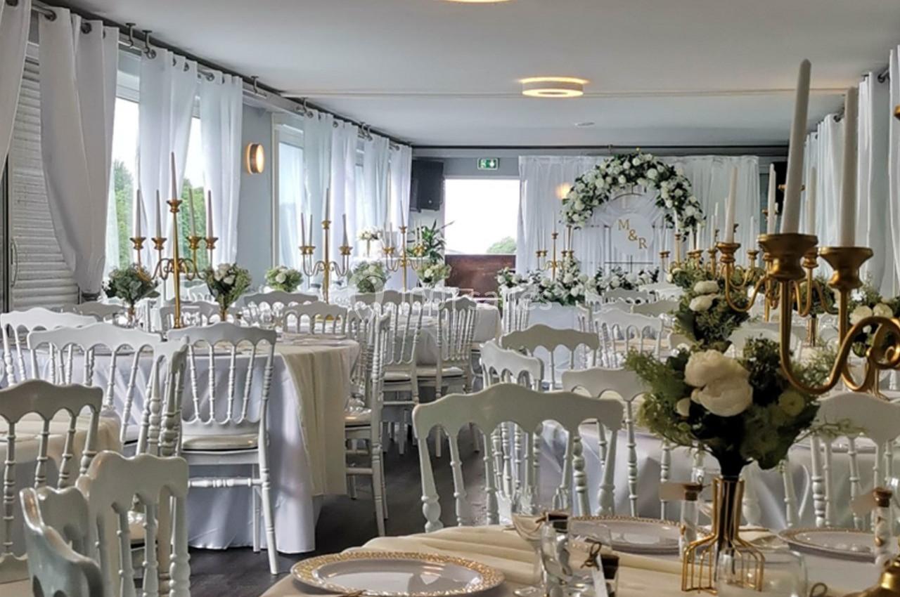 Salle de réception décorée pour un mariage avec des tables dressées, des chaises blanches et des arrangements floraux…