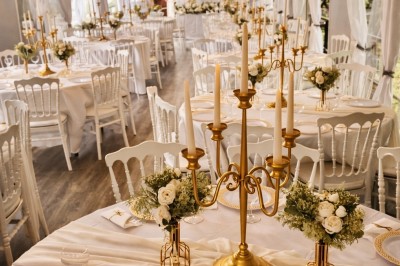 Table élégamment dressée avec nappes blanches, serviettes pliées, verres et décorations florales dans une salle lumineuse.