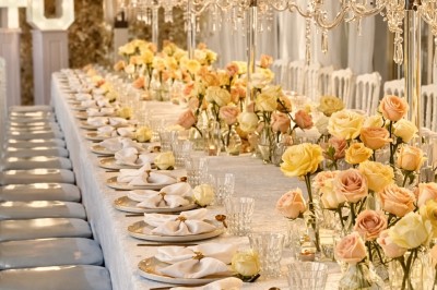 Table élégamment dressée avec nappes blanches, serviettes pliées, verres et décorations florales dans une salle lumineuse.